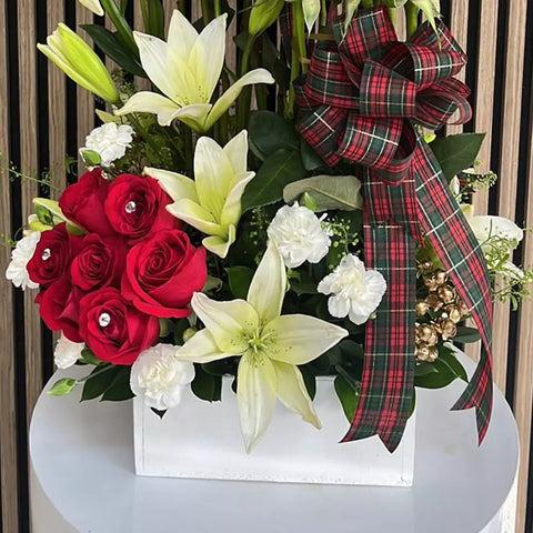 Imagen que muestra el detalle de los lirios y la base de madera. Flores de navidad en nuestra propuesta de arreglo con rosas y lirios para esta temporada, diseñado en una base de madera blanca con 18 rosas rojas y tres varas de lirios asiáticos. Tamaño del arreglo mediano. Floristería Flores 24 Horas.