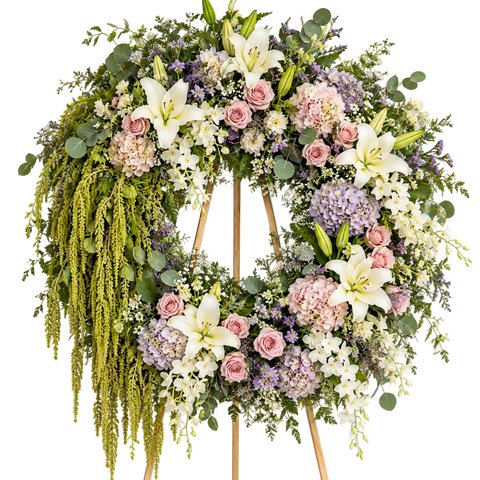 Corona fúnebre premium Jardín de Luz con rosas rosadas, lirios blancos, hortensias pastel y follajes colgantes, presentada sobre caballete de madera